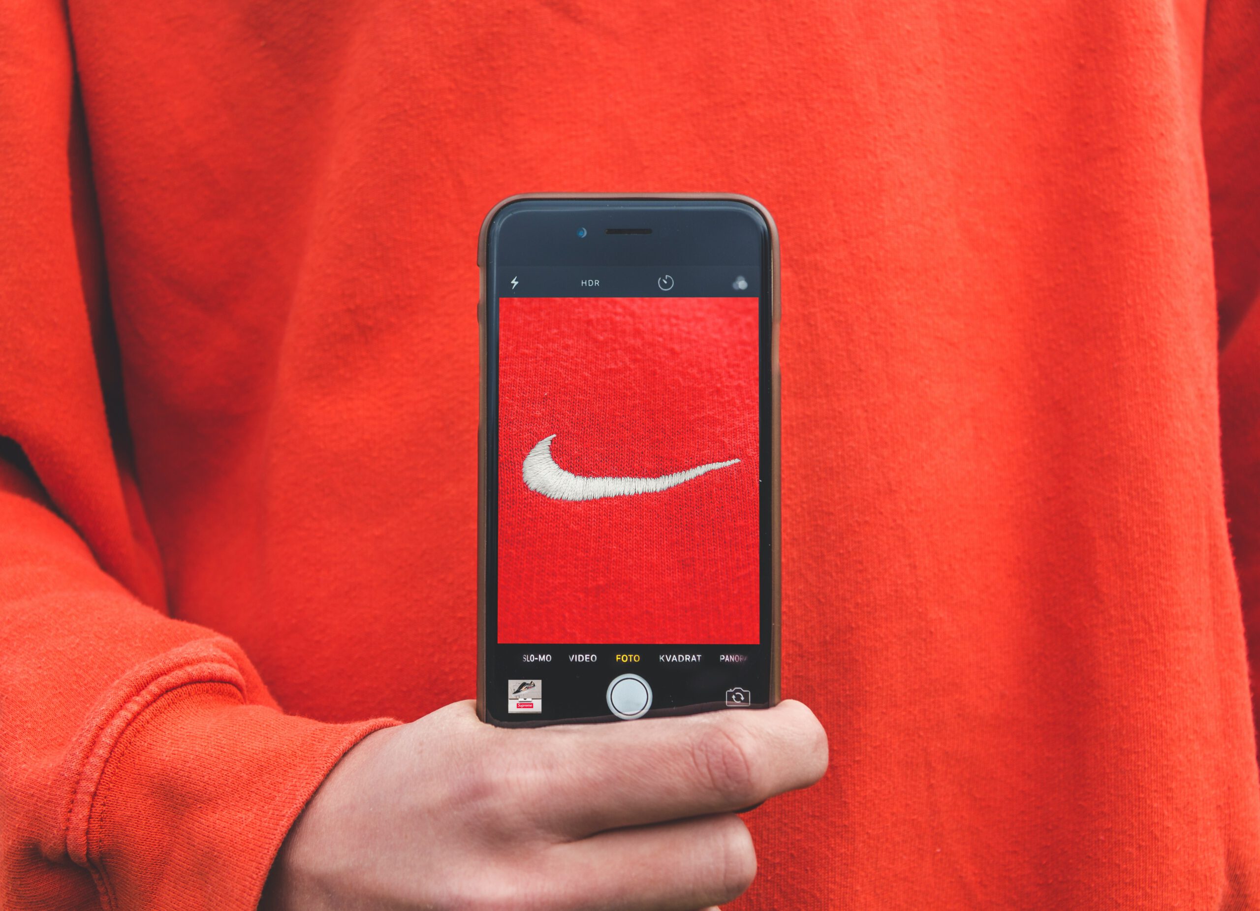 Bild eines Smartphones, das die geöffnete Kamera zeigt, welche den roten Nike-Pullover der Person dahinter zeigt. Stellvertretend steht das Bild für eine starke Brand Identity.